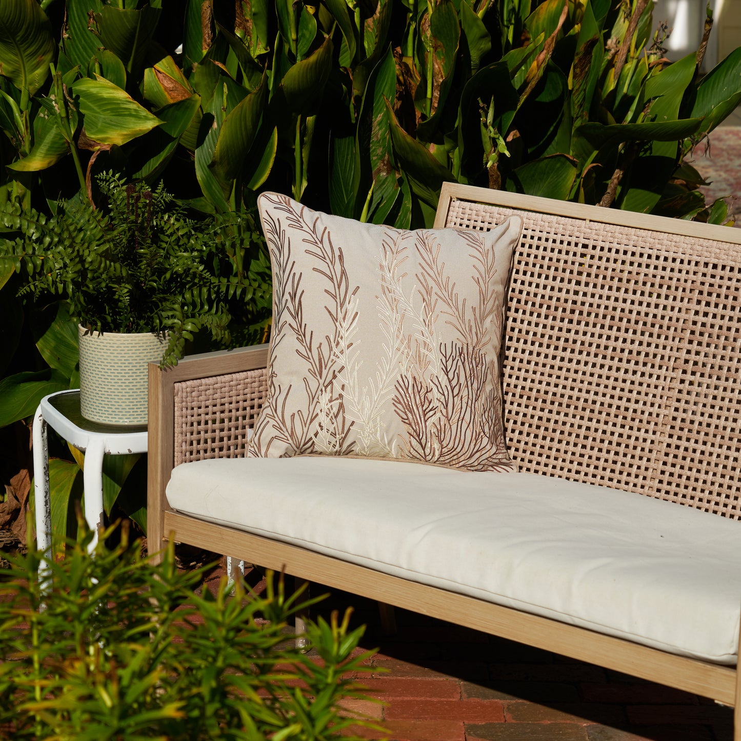Neutral Coral Pattern Embroidered Indoor Outdoor Pillow on a Bench Surrounded by Greenery