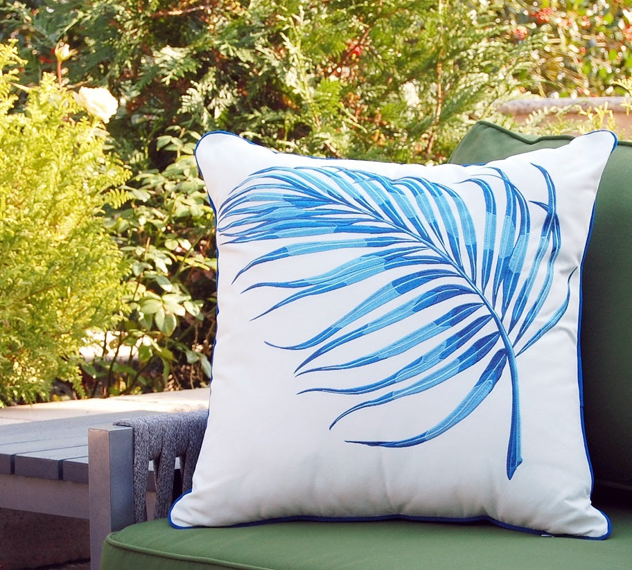 blue parlor palm leaf embroidered on white olefin pillow fabric sitting in a chair in a garden