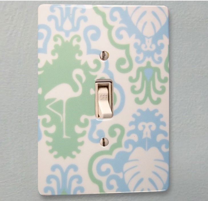 ceramic single toggle switchplate featuring printed green and light blue art deco design with palm leaf and flamingo silohuettes.