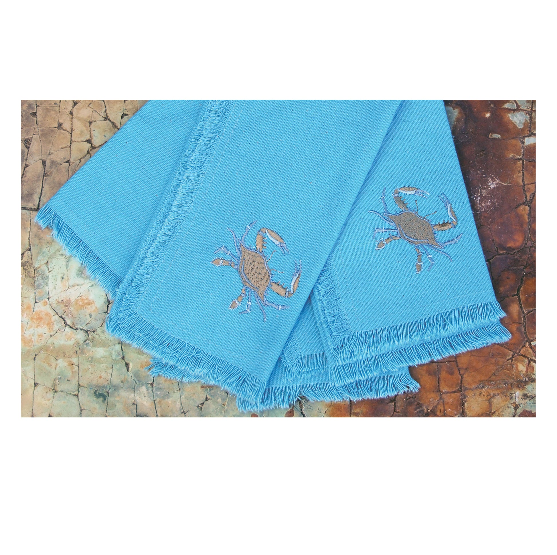 Blue crab embroidered on a coastal blue cotton napkin with fringe set of 4 stacked.
