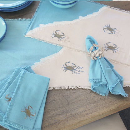 Baby blue crabs embroidered on sand colored ground and blue wave with embroidered sea foam placemat and runner. Blue crab embroidered on a coastal blue cotton napkin with fringe.