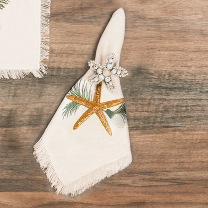 Natural cotton fringed napkin featuring an embroidered sea star and evergreen needles.