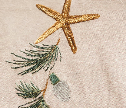 detailed view of embroidered sea stars, holiday lights, and evergreen needles on natural cotton fabric.