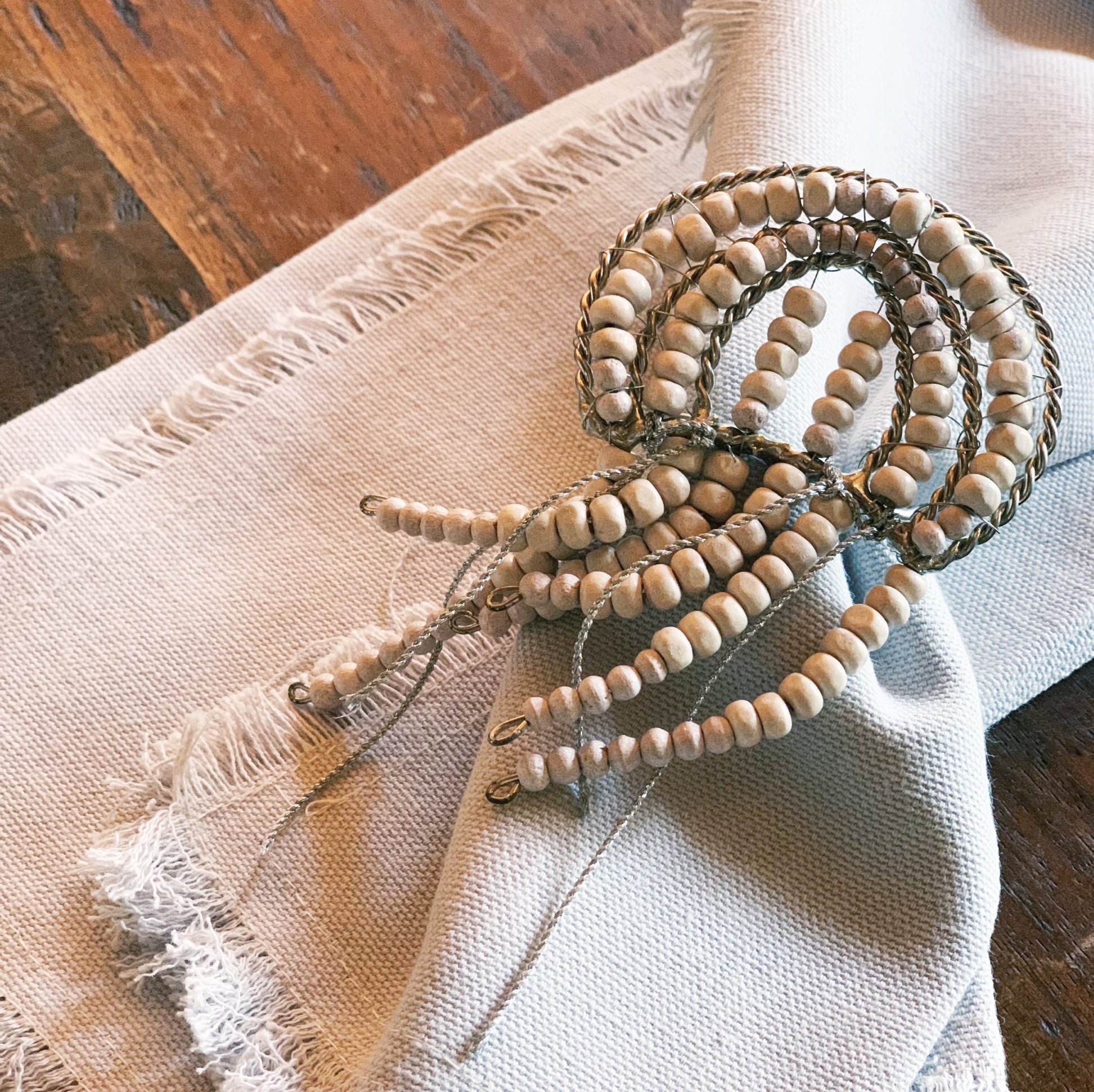 Jellyfish shaped napkin ring crafted of natural beads enclosing a natural cotton napkin.