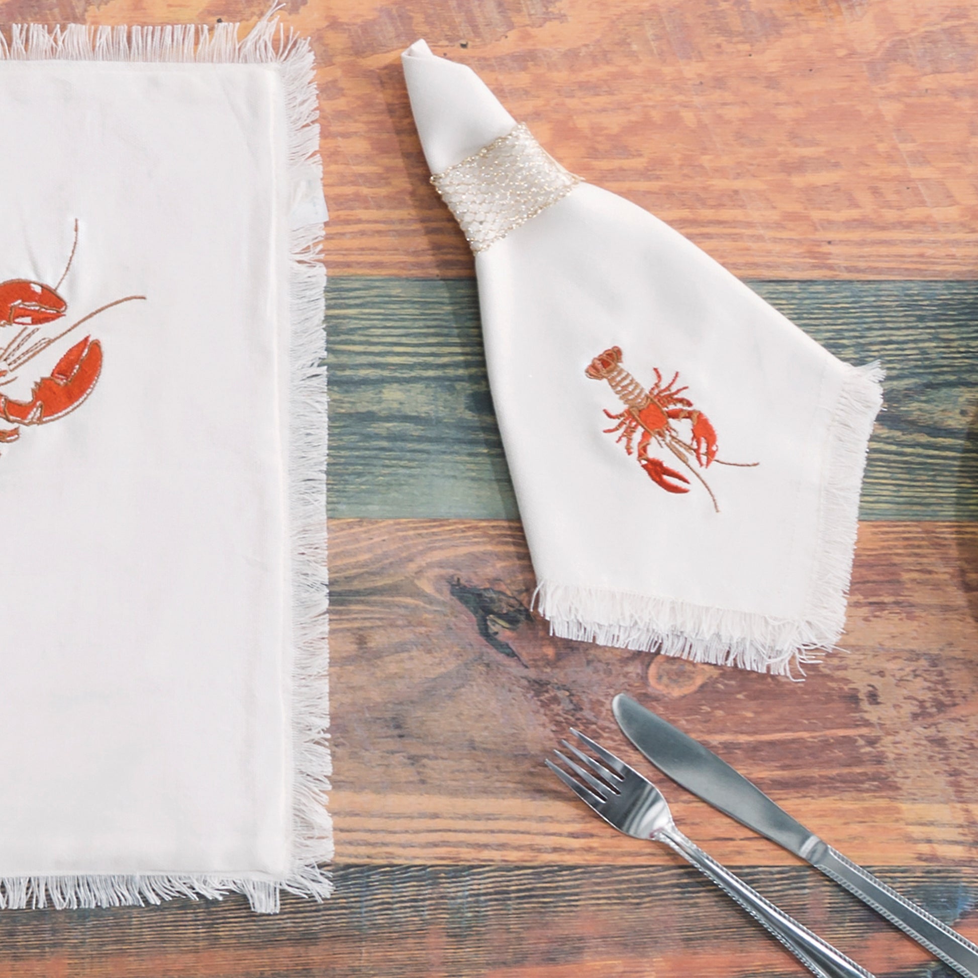 Natural fringed cotton table linens featuring embroidered red lobsters.