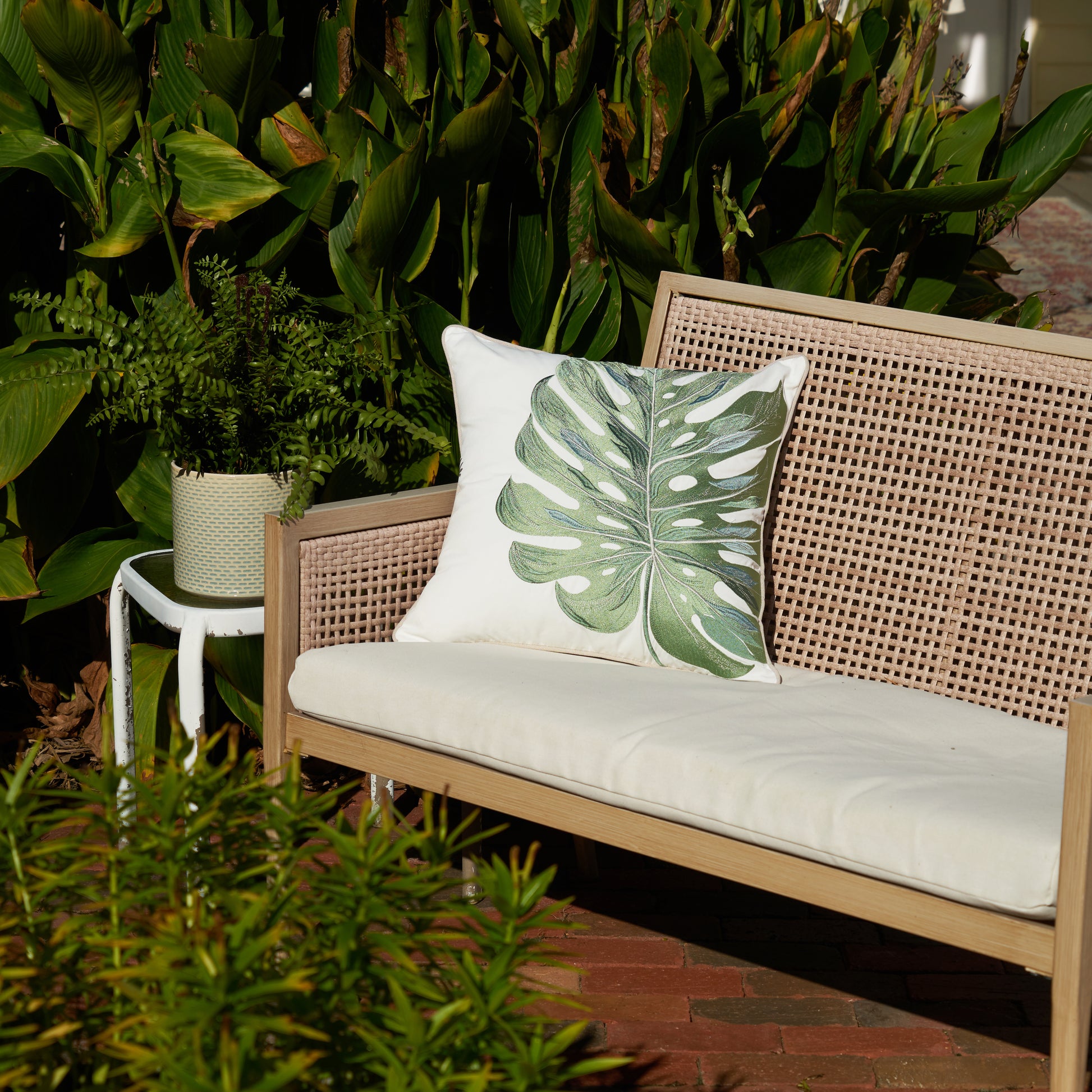 Sage Monstera Leaf Embroidered Indoor Outdoor Pillow on Bench Surrounded by Greenery