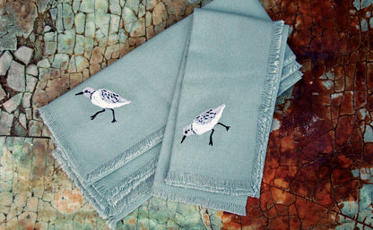 Set of 4 blue fringed cotton napkins with embroidered sandpiper adornment.