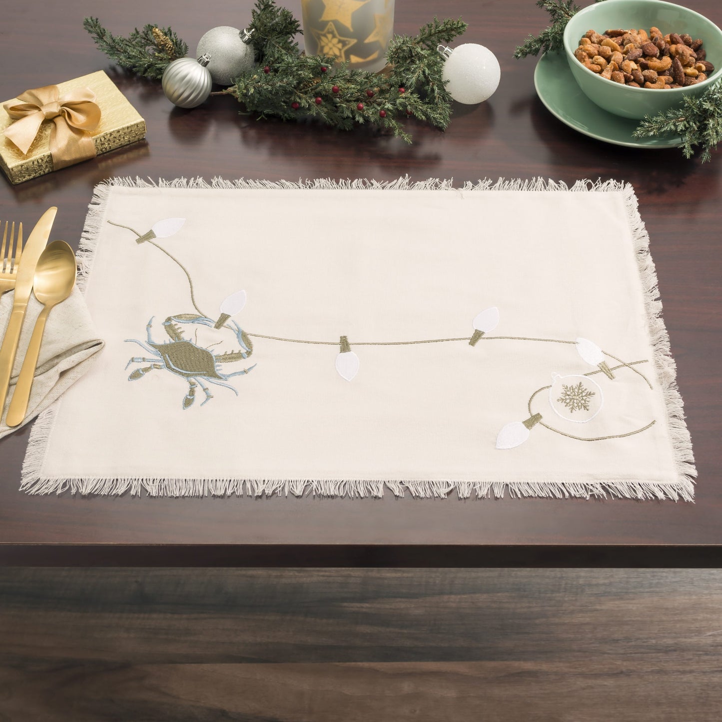 Holiday table setting featuring embroidered table linen collection features a blue crab and holiday lights on natural cotton with fringed edges. 