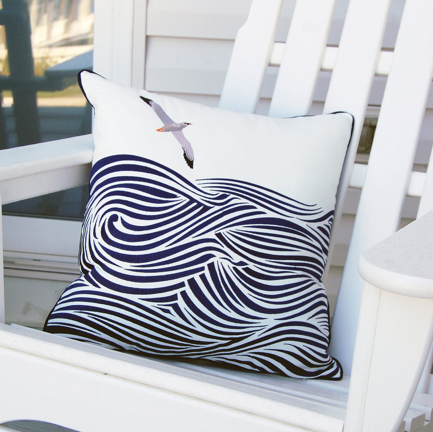 An albatross flying above blue lined waves embroidered on a white outdoor pillow..