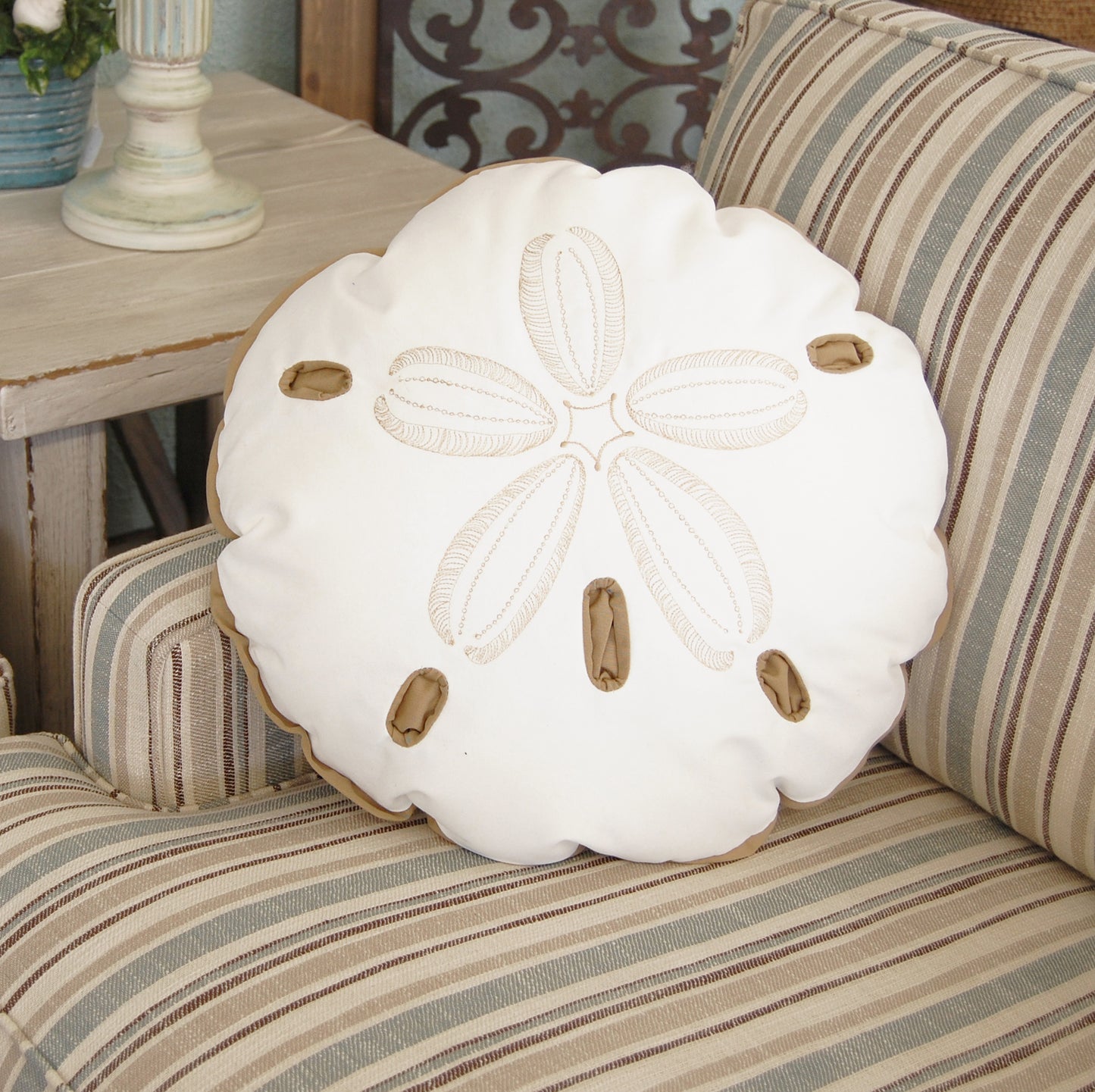Sand Dollar Shaped Beige Indoor Outdoor Pillow styled on a striped couch.