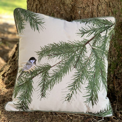 Chickadee and Bough pillow styled at the base of a pine tree.