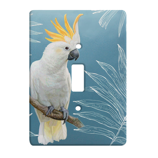 ceramic single toggle switch plate featuruing a white cockatoo bird sitting on a brach and a blue background with white outlined imagery of palm leaves. 