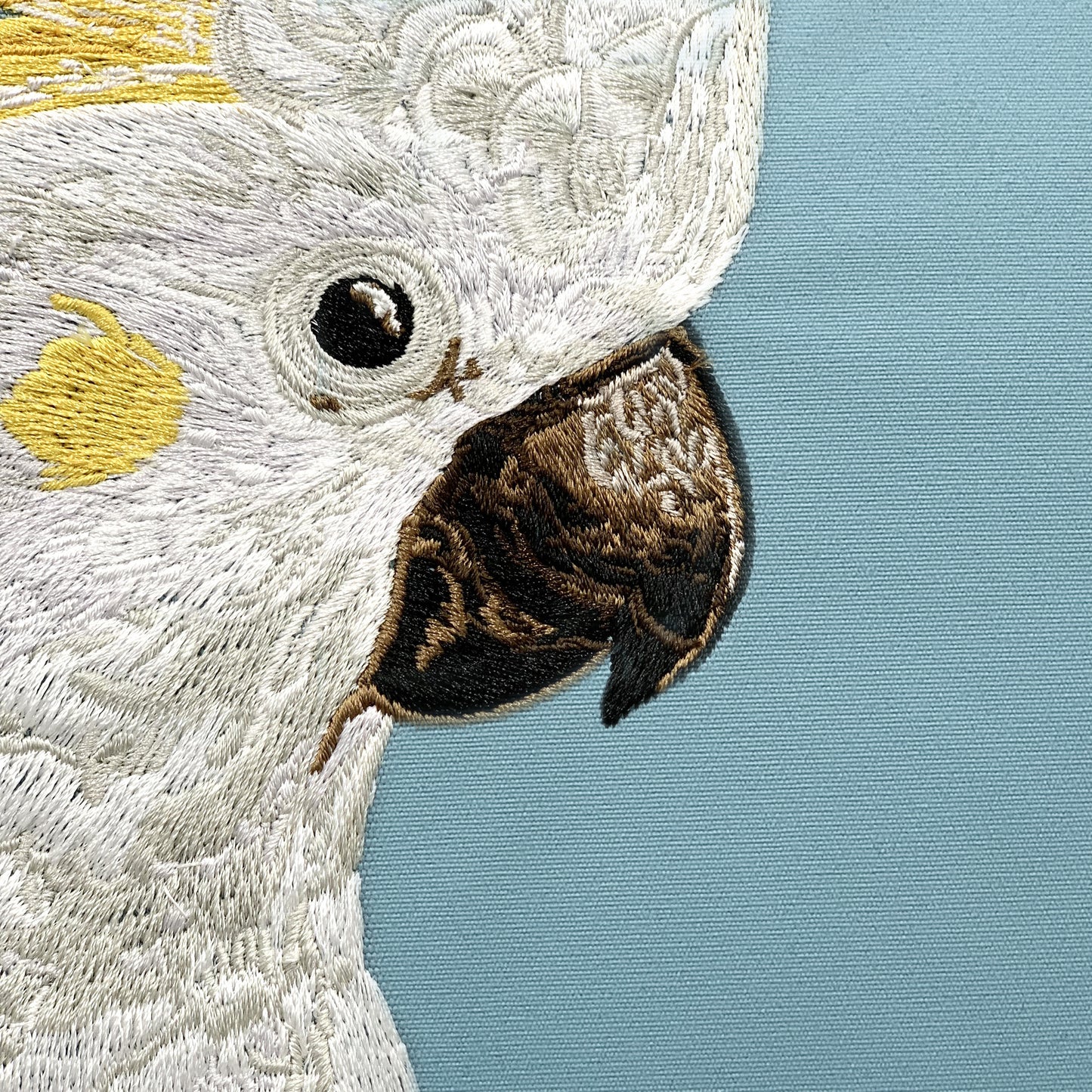 Detail shot of the Cockatoo and Leaves Indoor Outdoor Pillow embroidery.