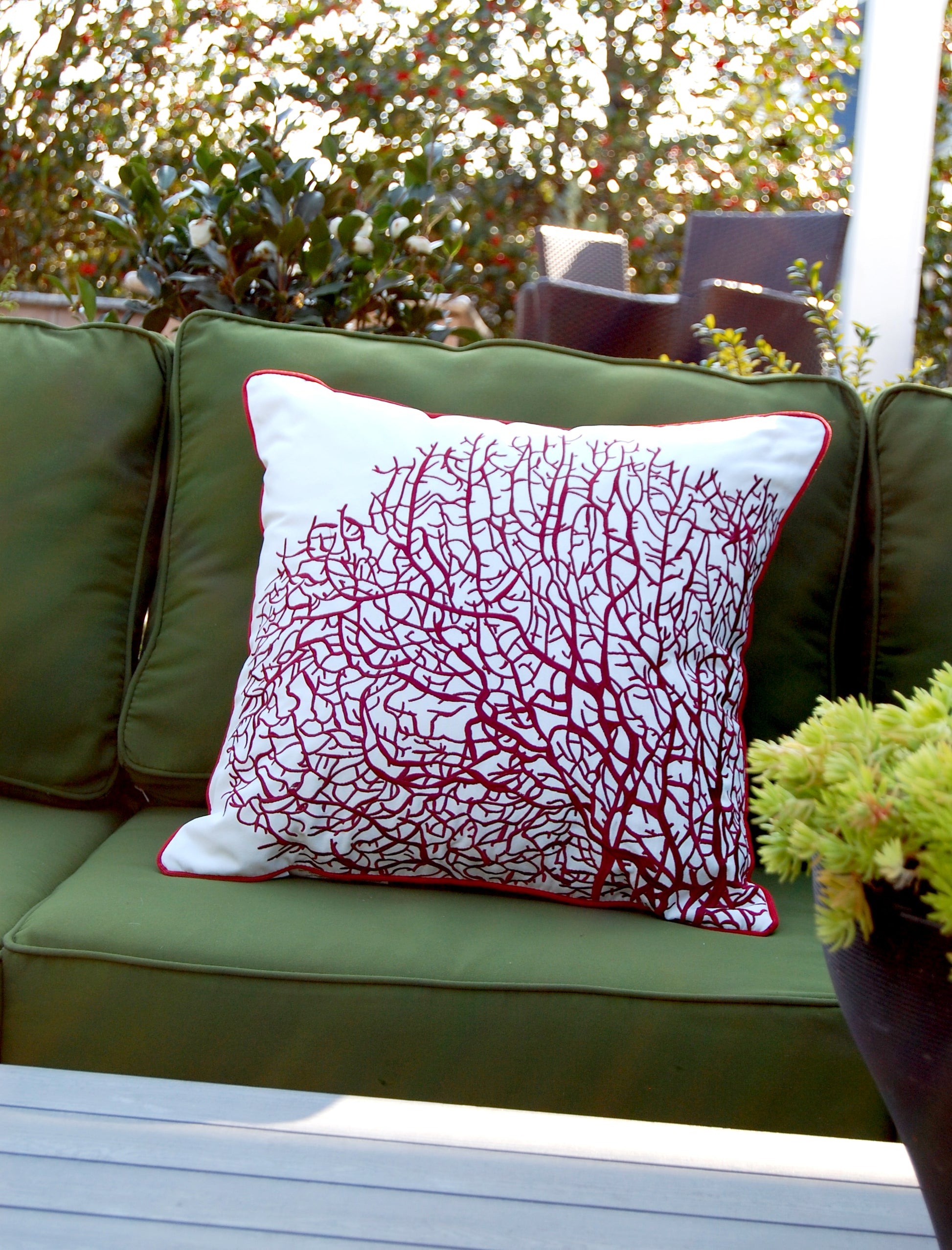 Fan Coral Red and White pillow styled on a green patio couch.
