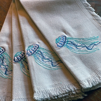 Navy and turquoise jellyfish embroidered on a grey cotton fringed napkin.