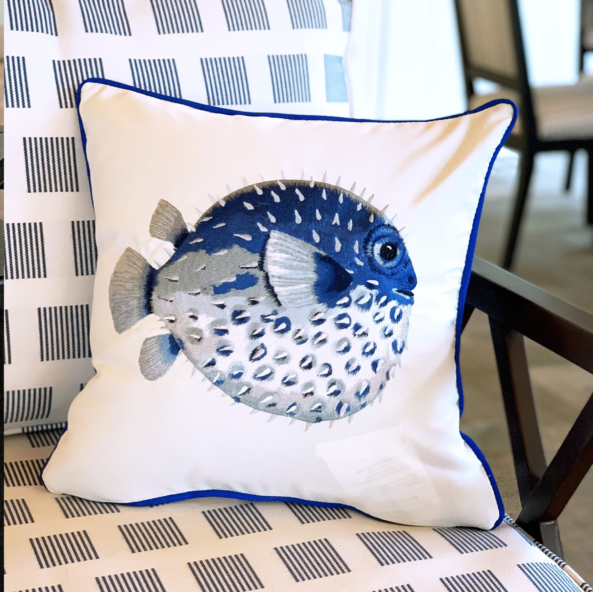 Blue Puffer Indoor Outdoor Pillow styled on an outdoor patio chair.