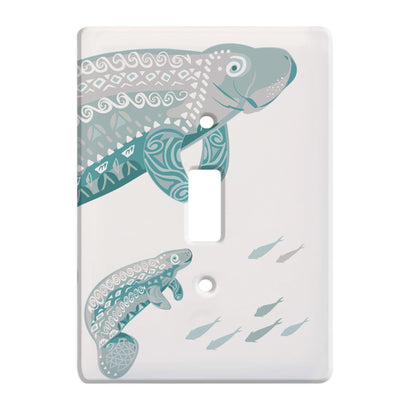 white ceramic single toggle switch plate featuring two teal manatees, one large one small. as well as a small group of fish swimming in the opposite direction.