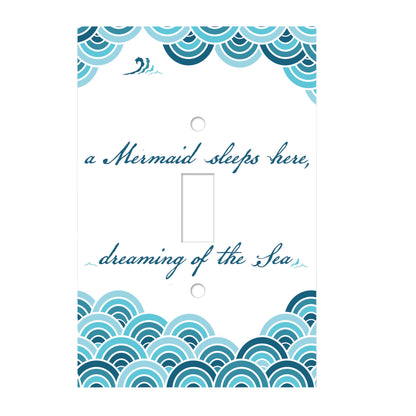 white ceramic single toggle switch plate featuring  blue script text that reads "a mermaid sleeps here, dreaming of the sea". also featured along the bottom and top edges of the switch plate are swirling blue accents.