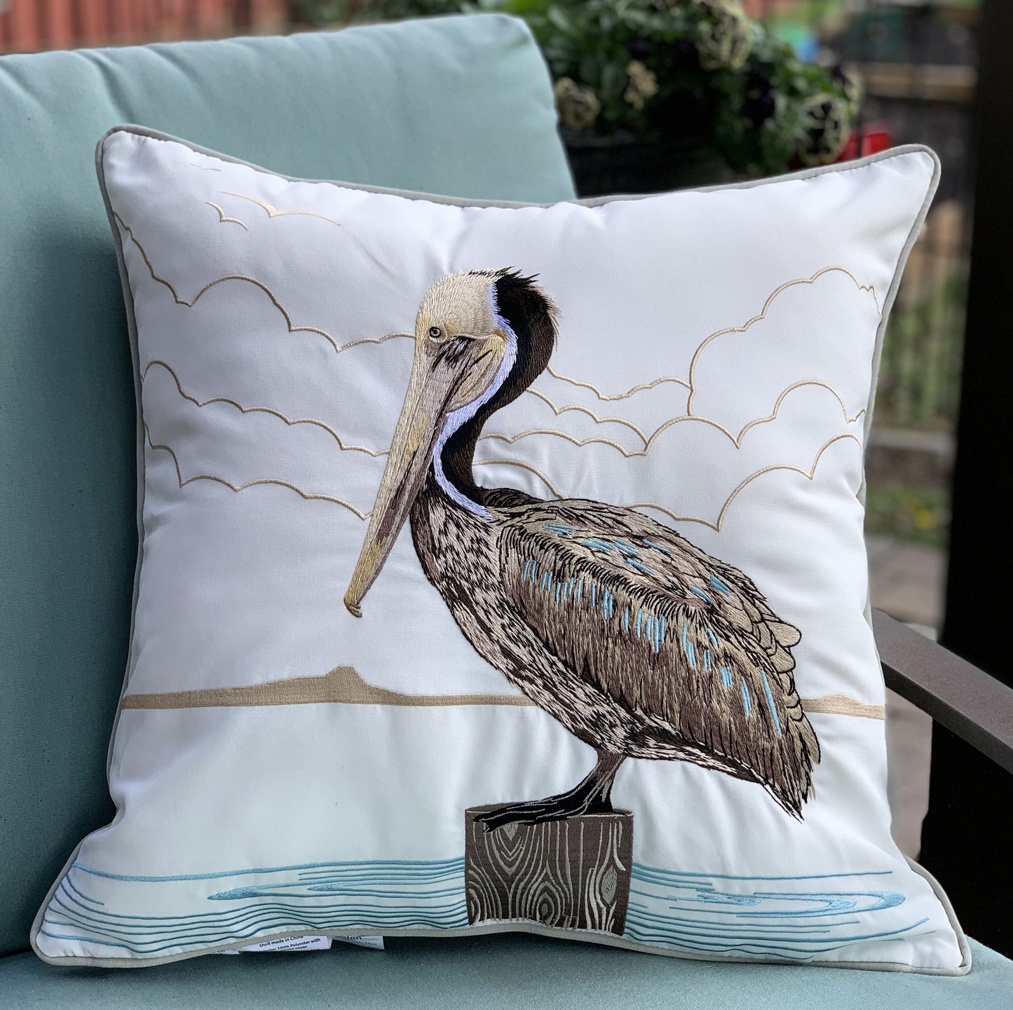 Sunbathing Brown Pelican Indoor Outdoor Pillow styled on a patio chair.