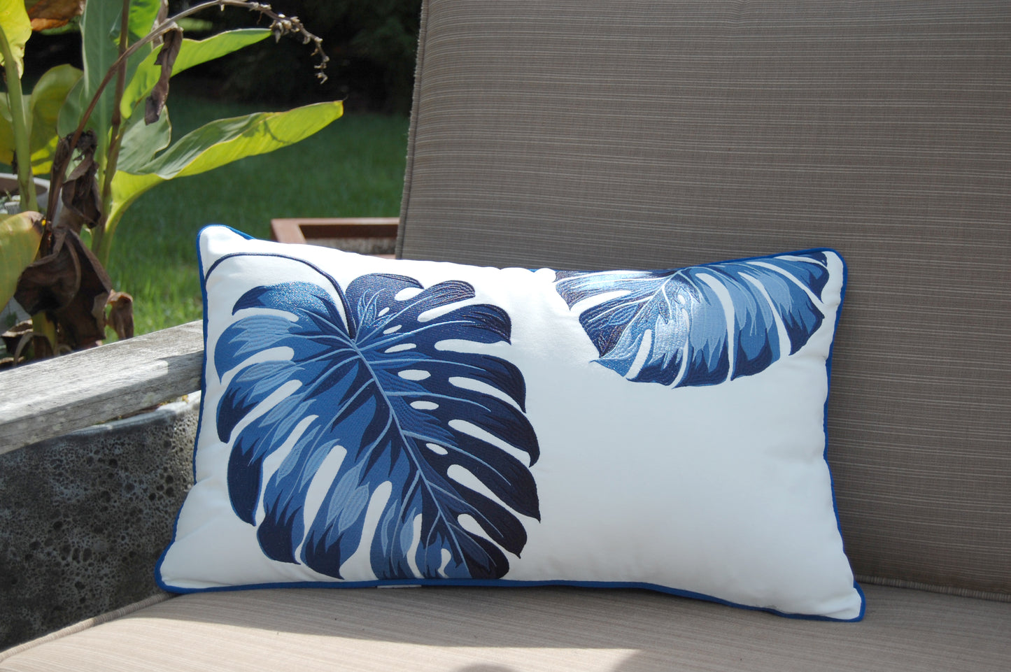 Blue Monstera Lumbar Indoor Outdoor Pillow styled on a patio chair.