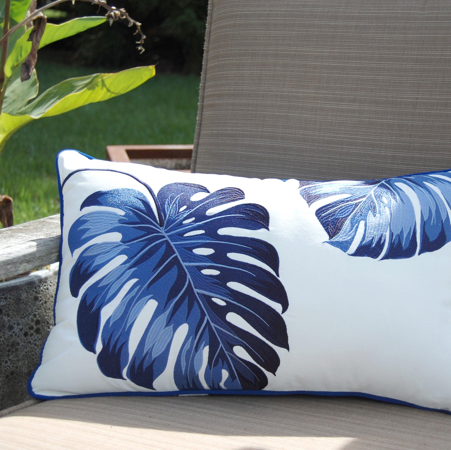 Blue Monstera Lumbar Indoor Outdoor Pillow styled on a patio chair.