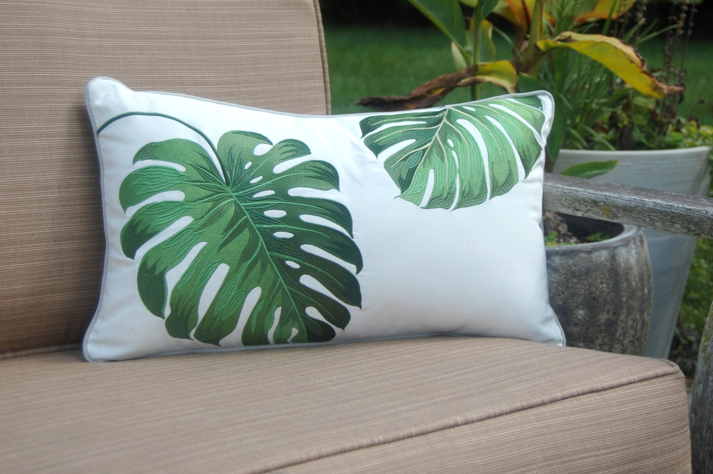 Green Monstera Lumbar Indoor Outdoor Pillow styled on a patio chair.