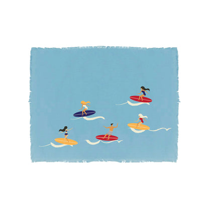 Embroidered placemat in a cool coastal blue featuring fringed edges. Multicolored embroidery scene with a bird’s eye view of a pack of surfer’s riding the waves.